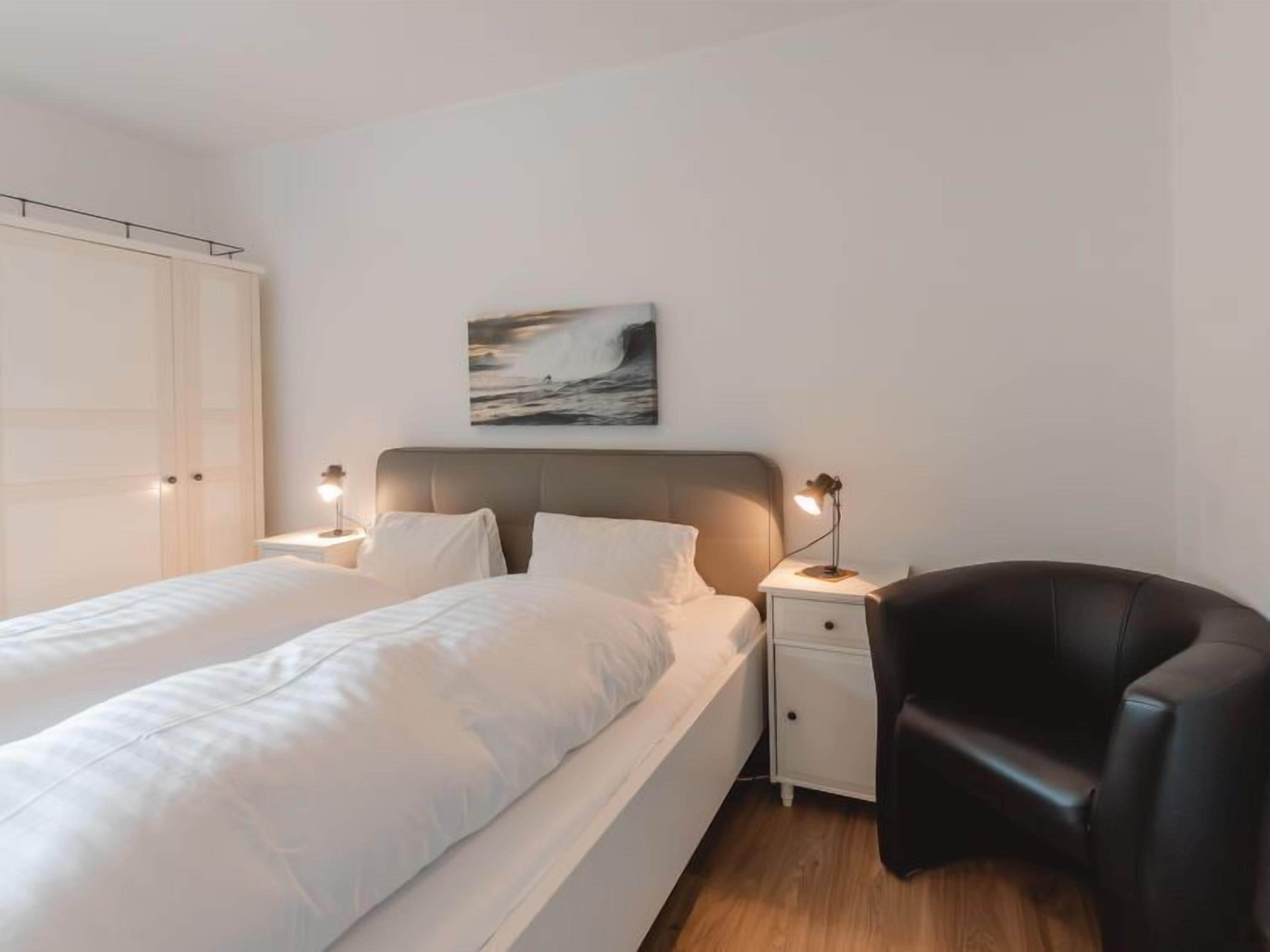 A bedroom with a bed, bedside tables, a chair, and a painting on the wall.