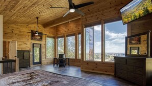 Una habitación amplia con ventanas grandes, ventilador de techo y cama con colcha estampada.