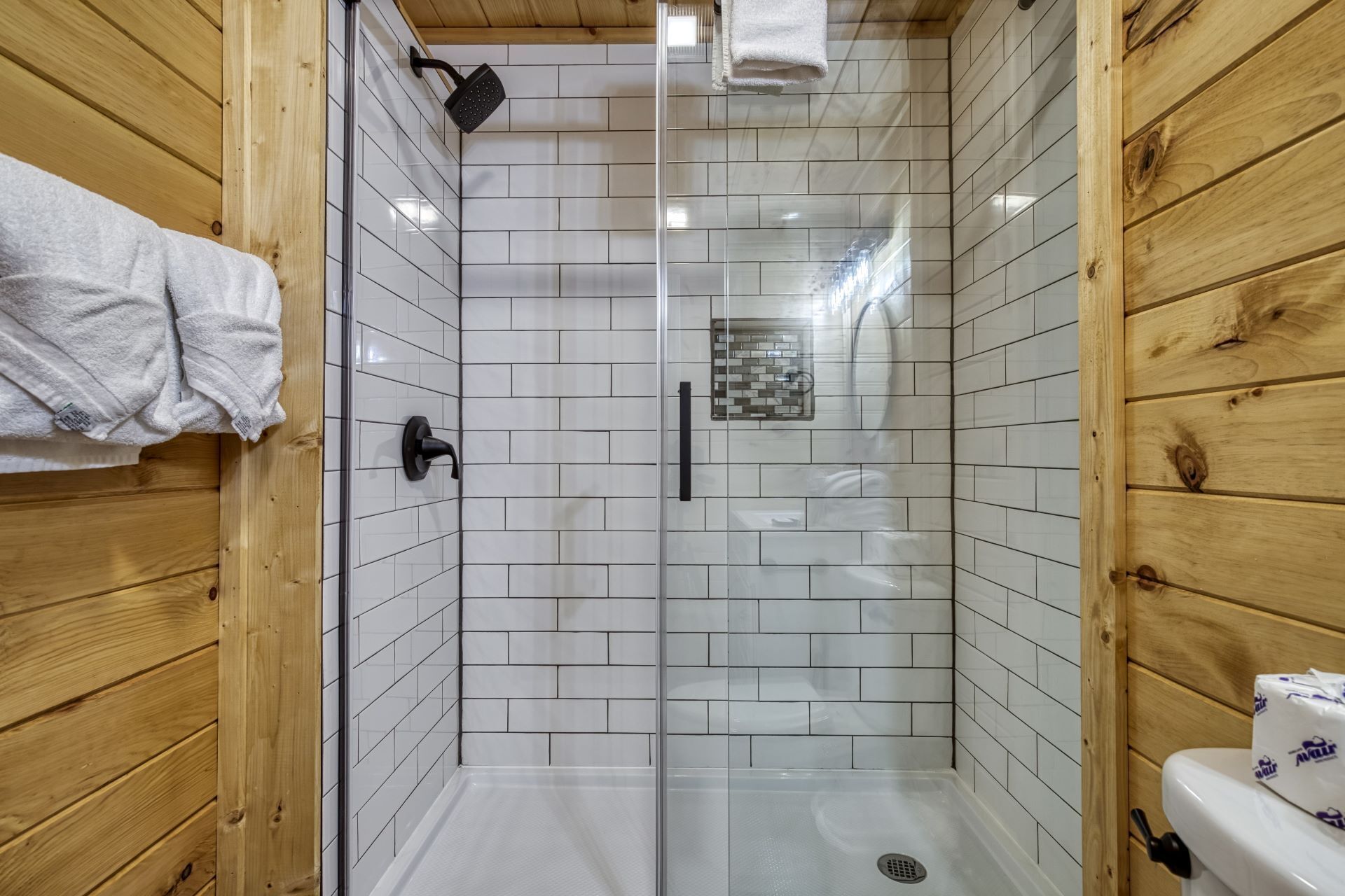 A shower with white tiles, a glass door, and wooden walls.