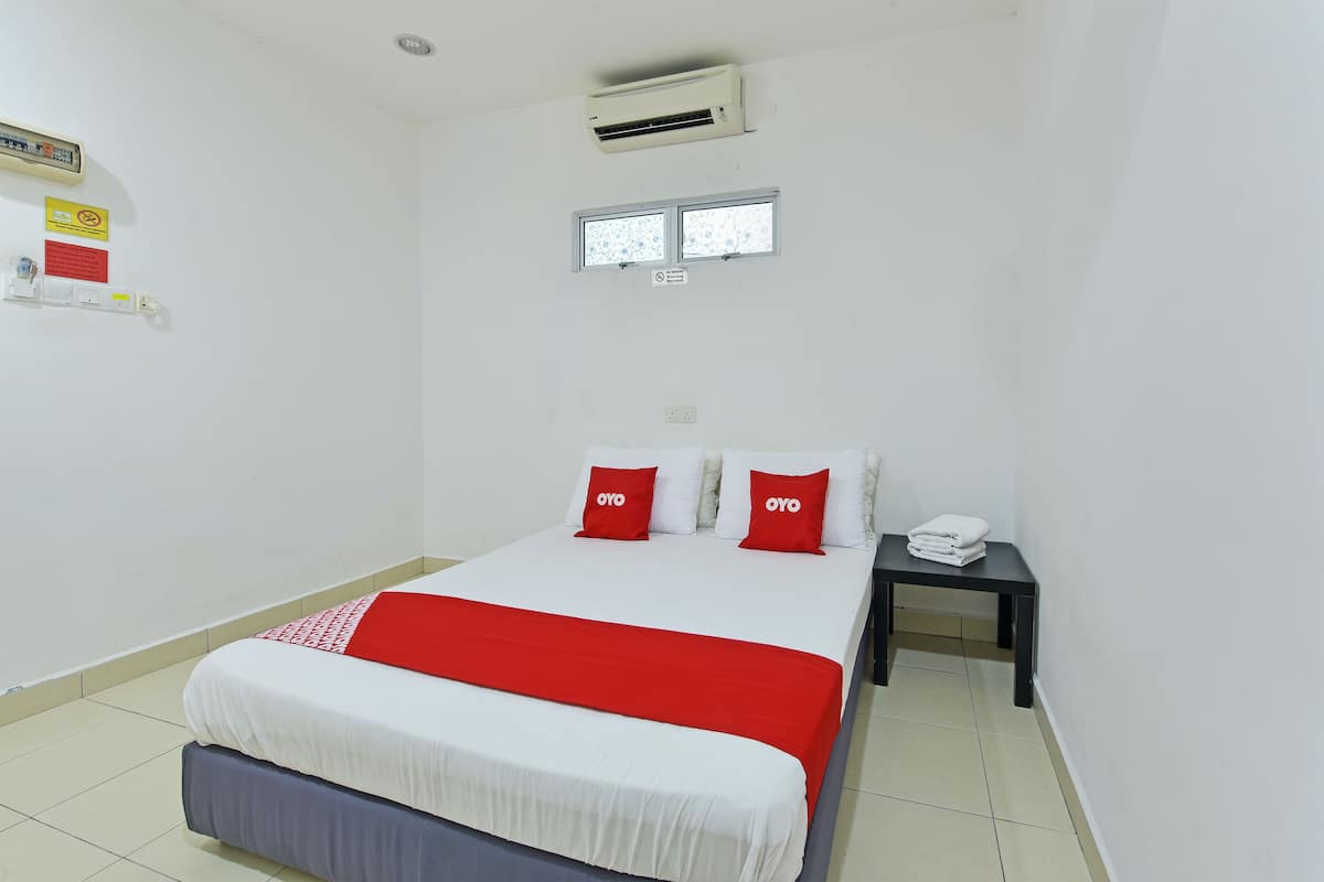 A hotel room with a bed, a nightstand, an air conditioner, and a window.