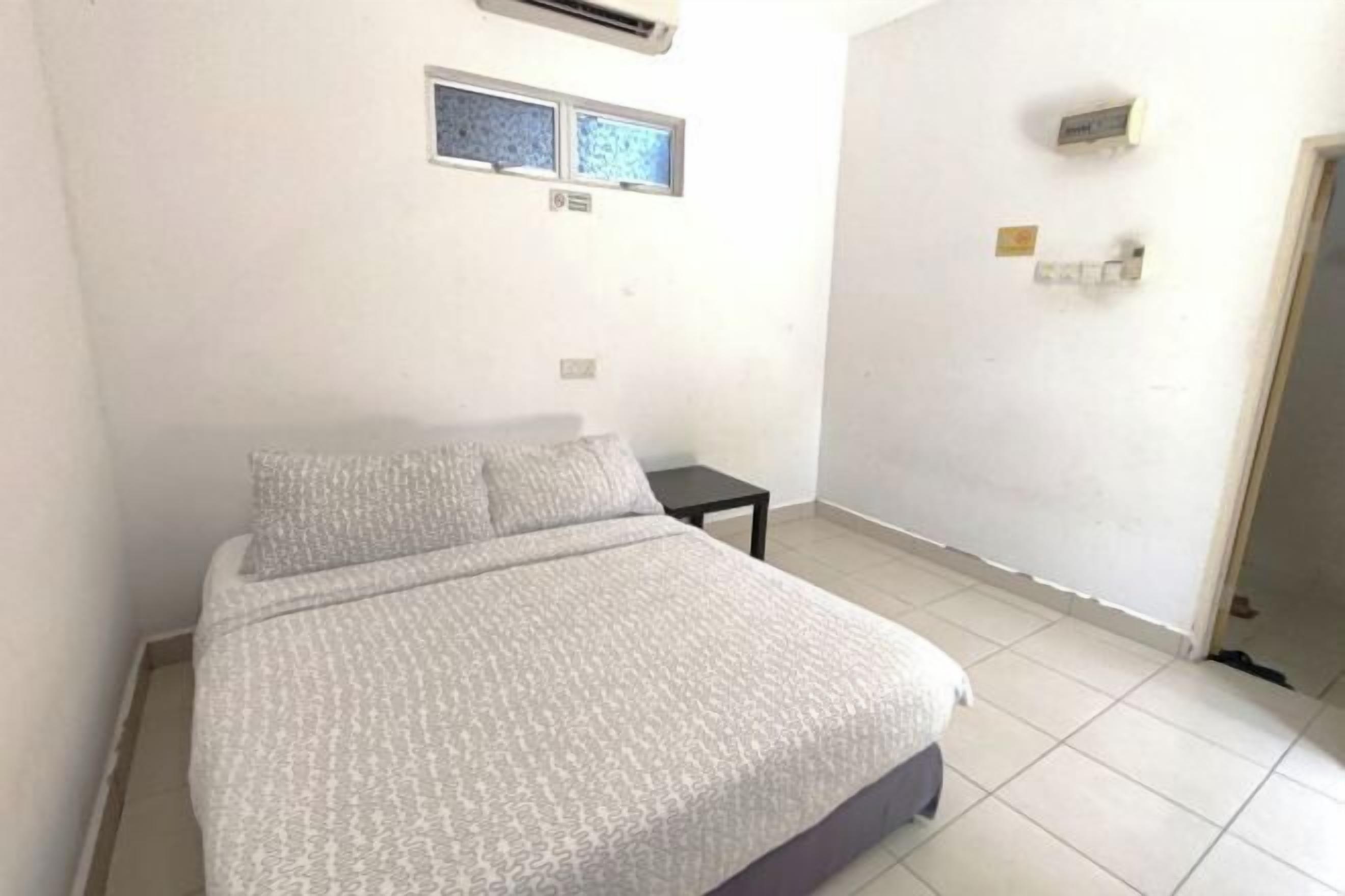 A bedroom with a bed, a small table, and a wall-mounted air conditioner.