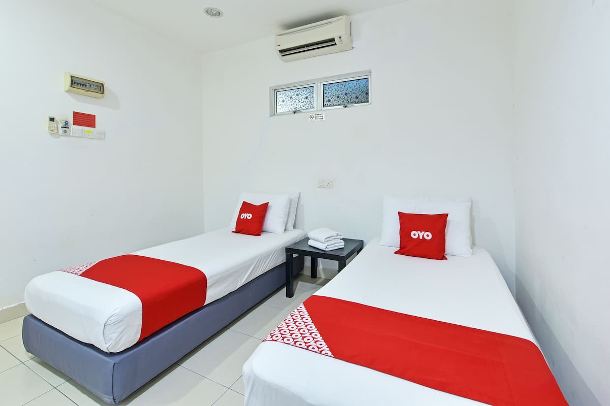A hotel room with two beds, each with a red and white bedspread, a small table with a telephone, and a wall-mounted air conditioner.