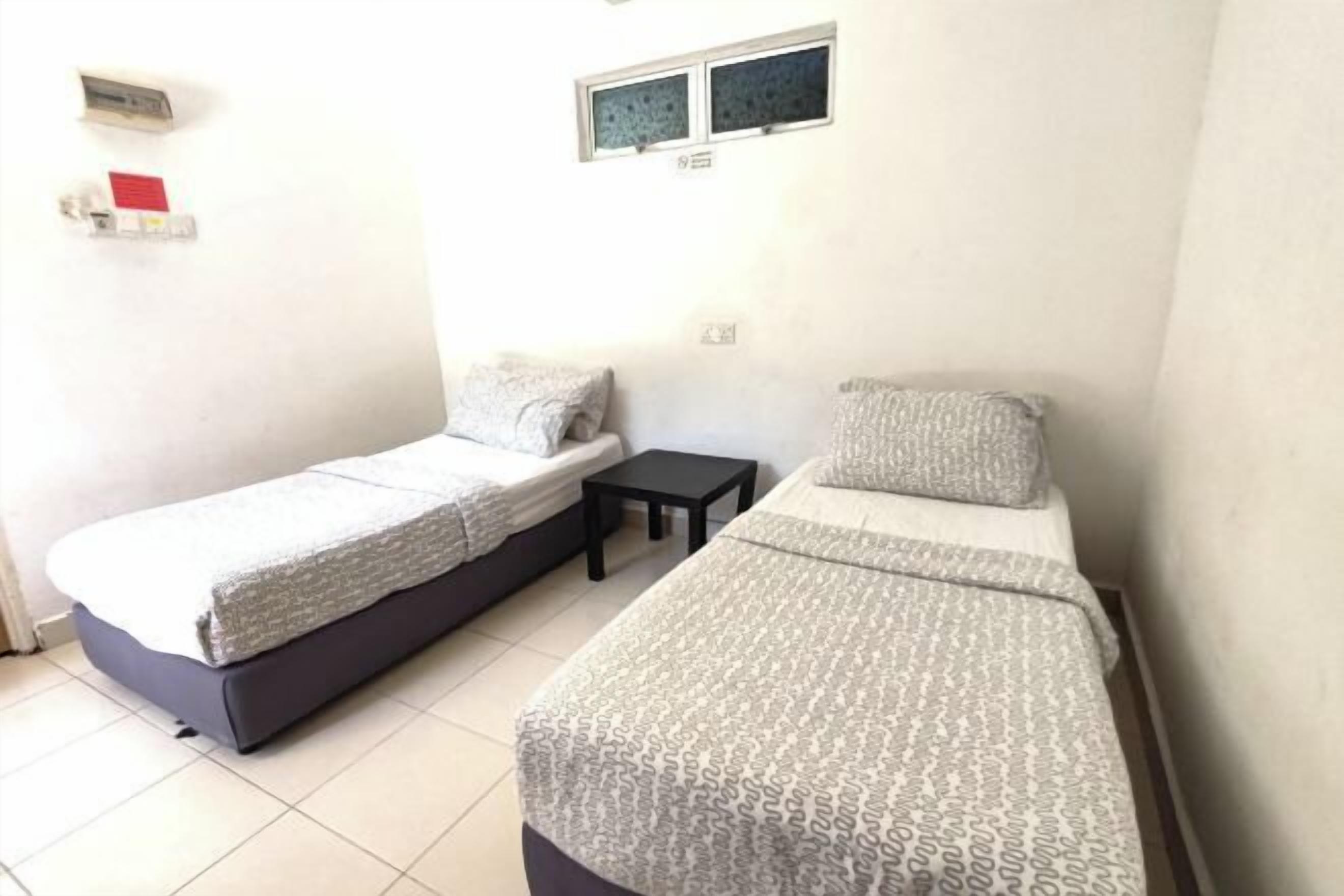 A small, clean room with two single beds, a small table, and a window.