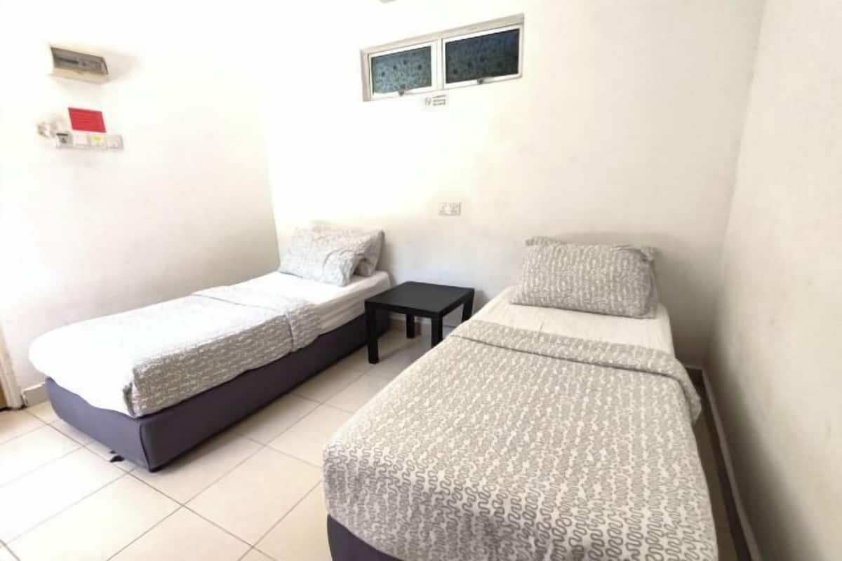 A small, clean room with two single beds, a small table, and a window.