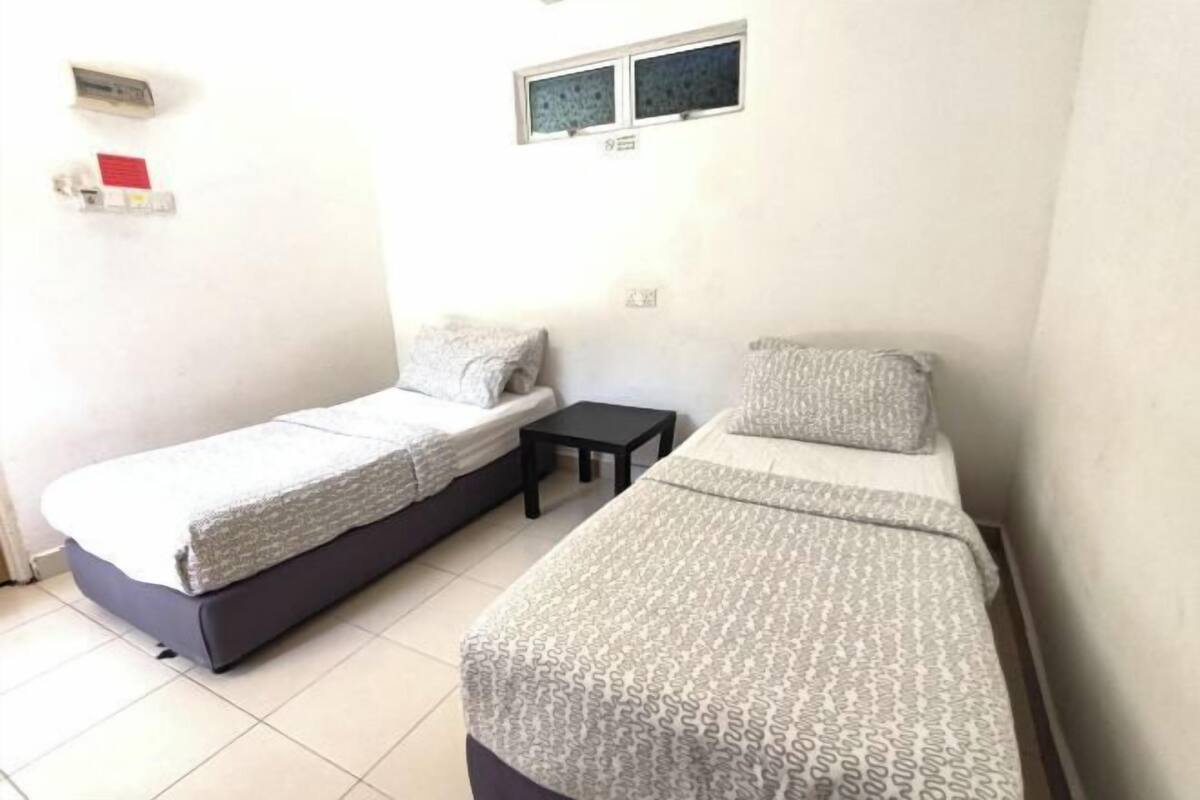 A small, clean room with two single beds, a small table, and a window.
