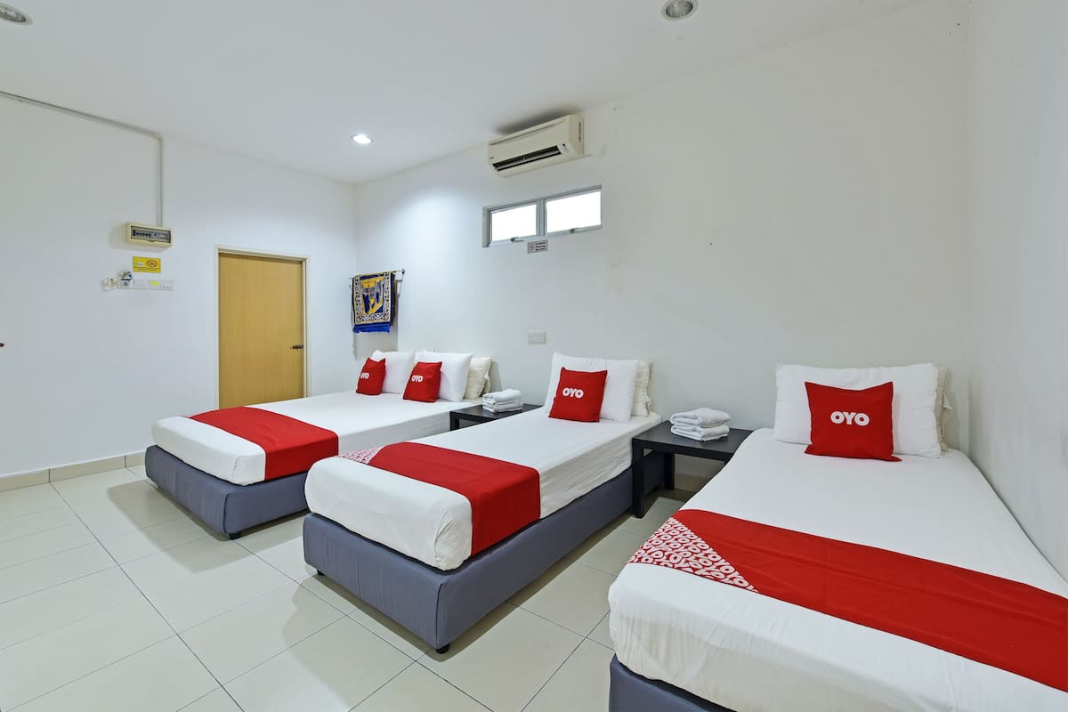 A hotel room with three beds, each with red and white bedding, a small table with a phone, and a door.