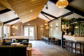 A spacious hotel lobby with a high ceiling, wooden paneling, and a bar area with stools. - De Jister Groepshuis aan het Water Voor 30-62 Personen (Nes)