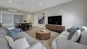 Un salon moderne avec un canapé gris, une table basse en bois, un téléviseur et un coin repas comprenant une table et des chaises.