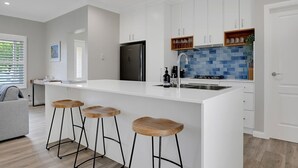 Une cuisine moderne avec des meubles blancs, un réfrigérateur noir, un pare-feu en carreaux bleus et des tabourets en bois.