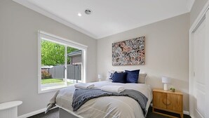 Une chambre à coucher comprenant un lit, une fenêtre, une table de chevet et une œuvre d’art murale.