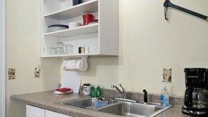 Una cocina con encimera de granito, pileta de acero inoxidable, muebles blancos y cafetera.