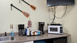 Una cocina con microondas, cafetera y estación para café. Hay dos paletas de madera colgadas en la pared.