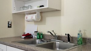 Eine Küche mit zwei Edelstahl-Spülen, einem weißen Schrank darüber und einer Arbeitsplatte mit einem roten Tuch und Reinigungsmitteln.