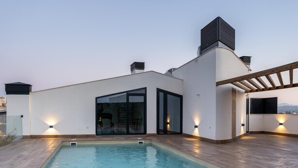 Una piscina en la azotea con diseño moderno, rodeada por una terraza de madera y paredes blancas.