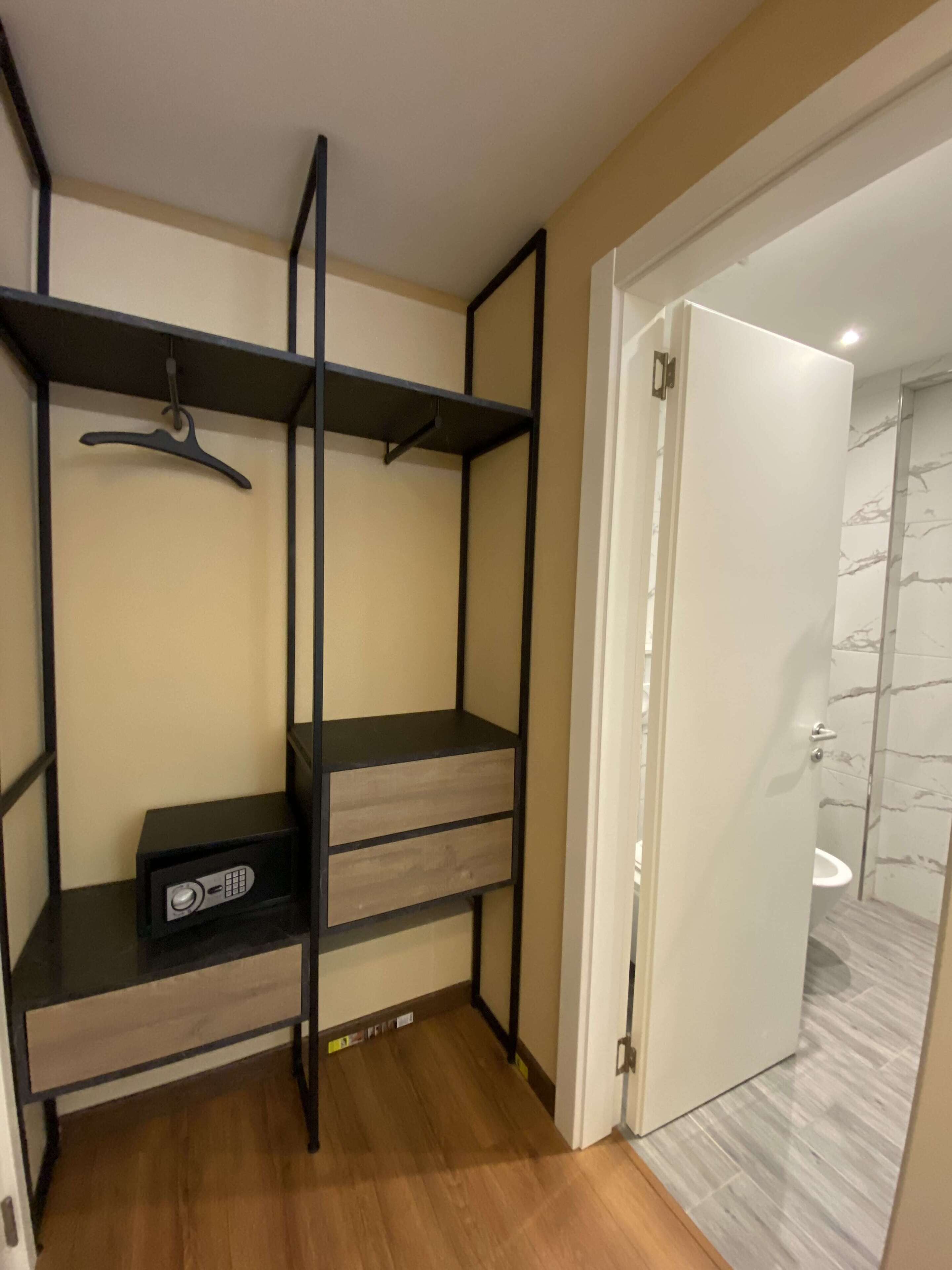 A compact room with a built-in wardrobe, a small desk with drawers, and a door leading to a bathroom with a marble backsplash.