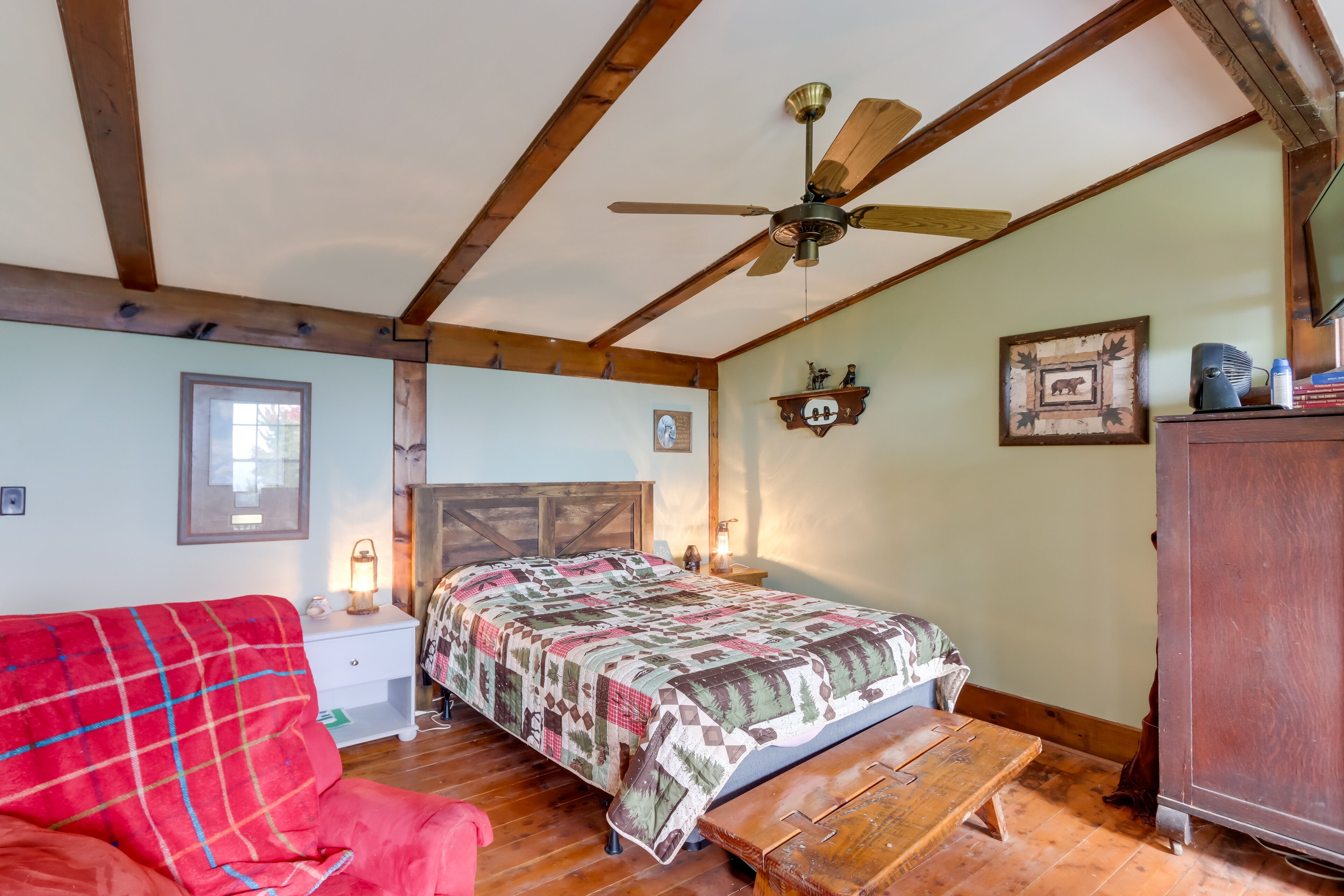 Une chambre confortable avec un lit, un banc en bois, une chaise rouge, un ventilateur de plafond et une commode.