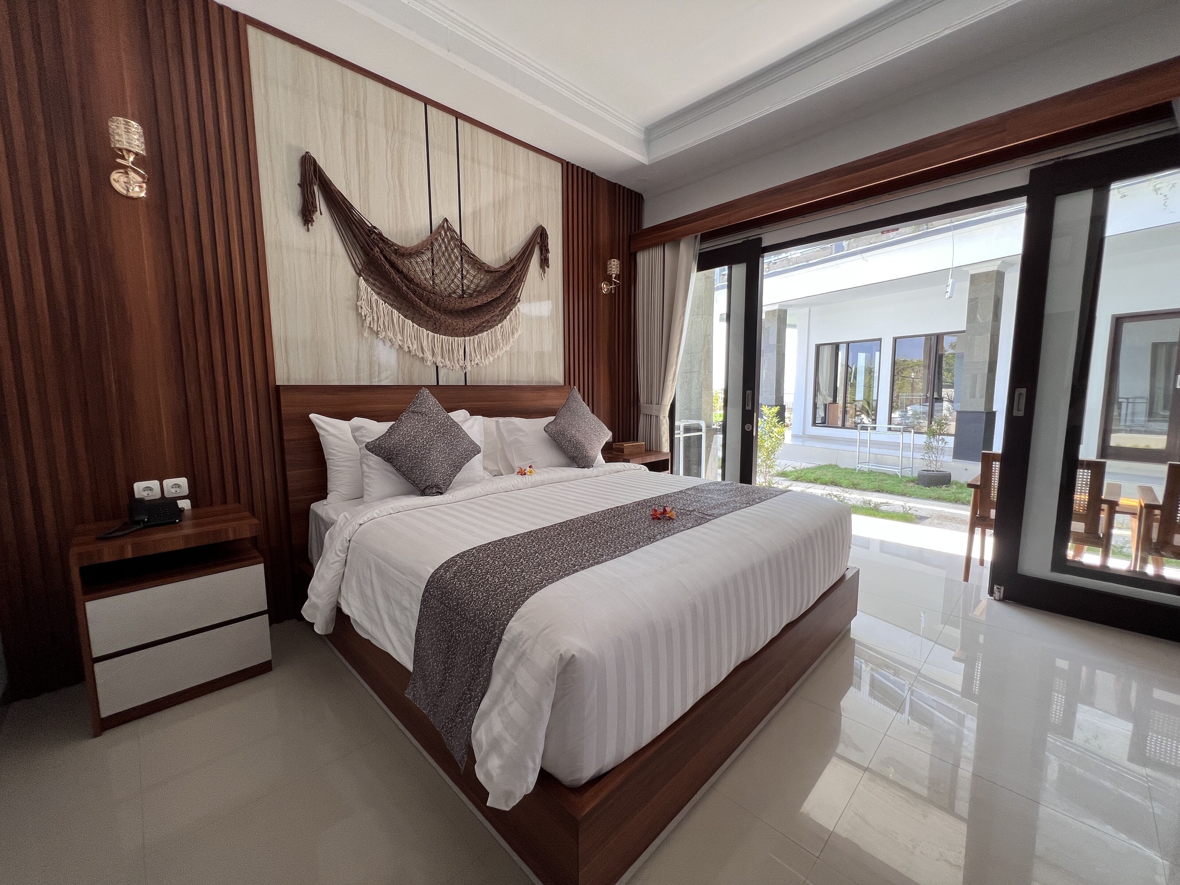 A modern bedroom with a large bed, wooden paneling, a hammock, and a view of the outside.