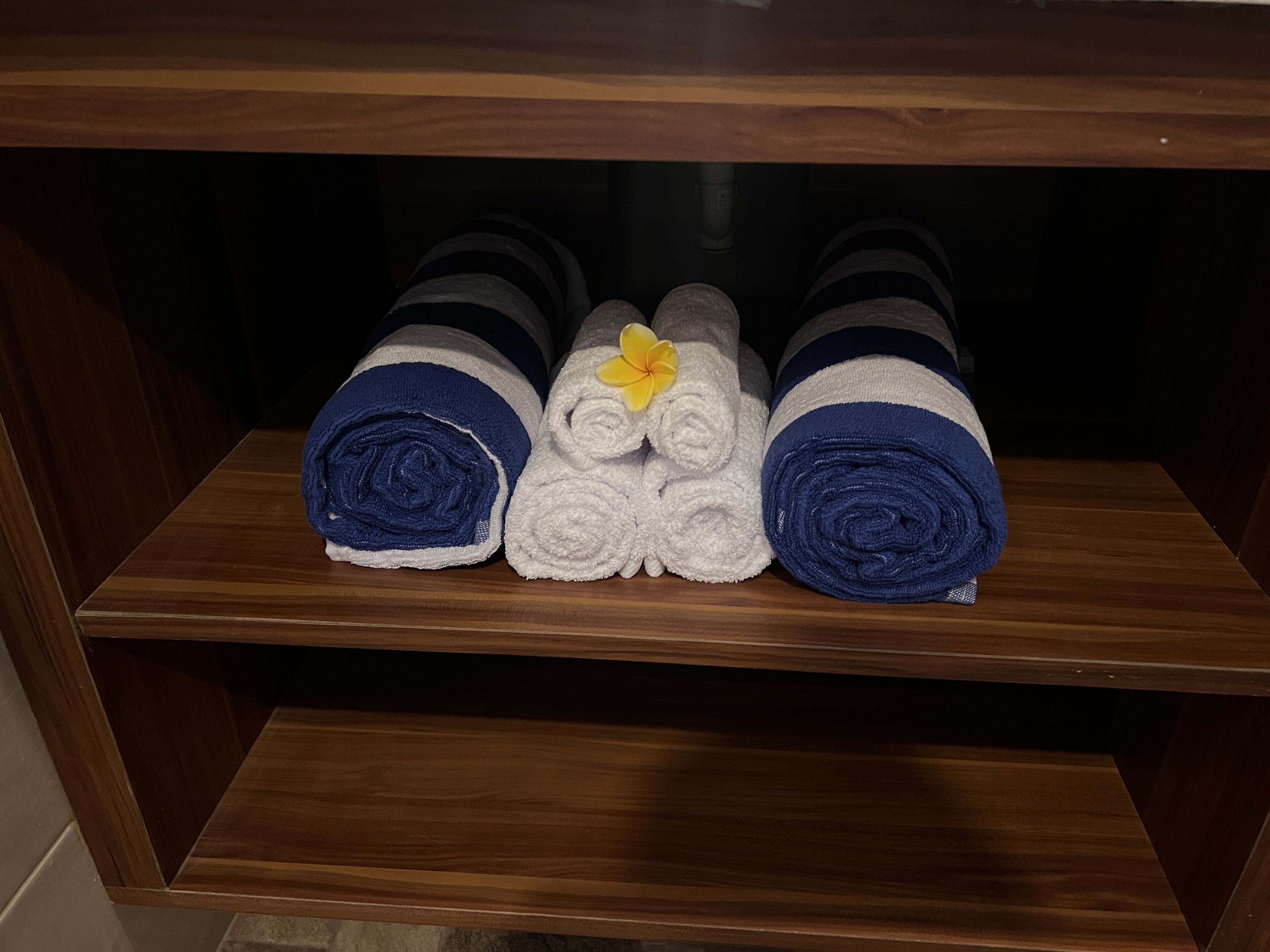 A wooden shelf with three rolled towels, one with a yellow flower.