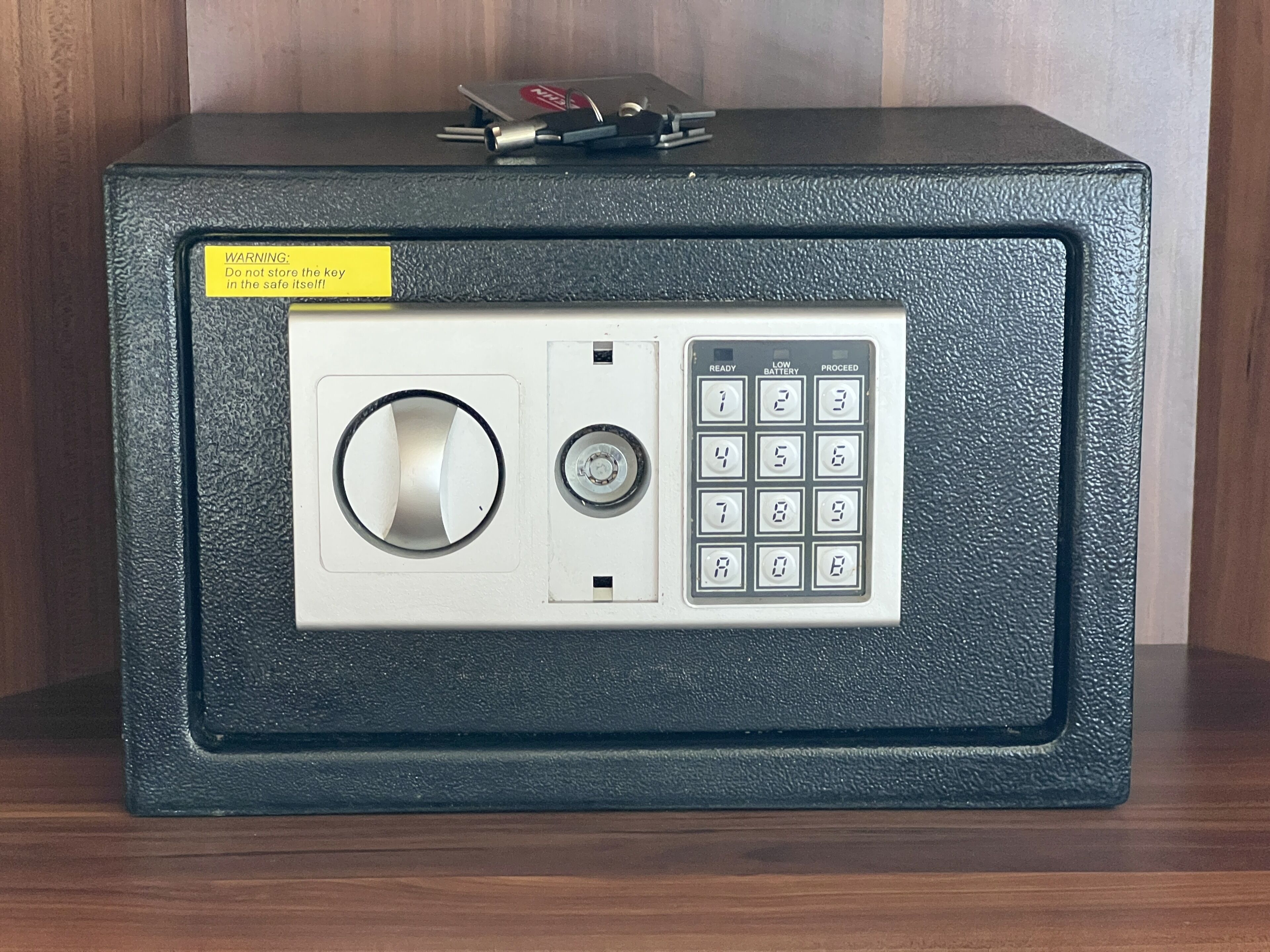 A safe with a keypad and a keyhole, a warning label, and a small set of keys on top.