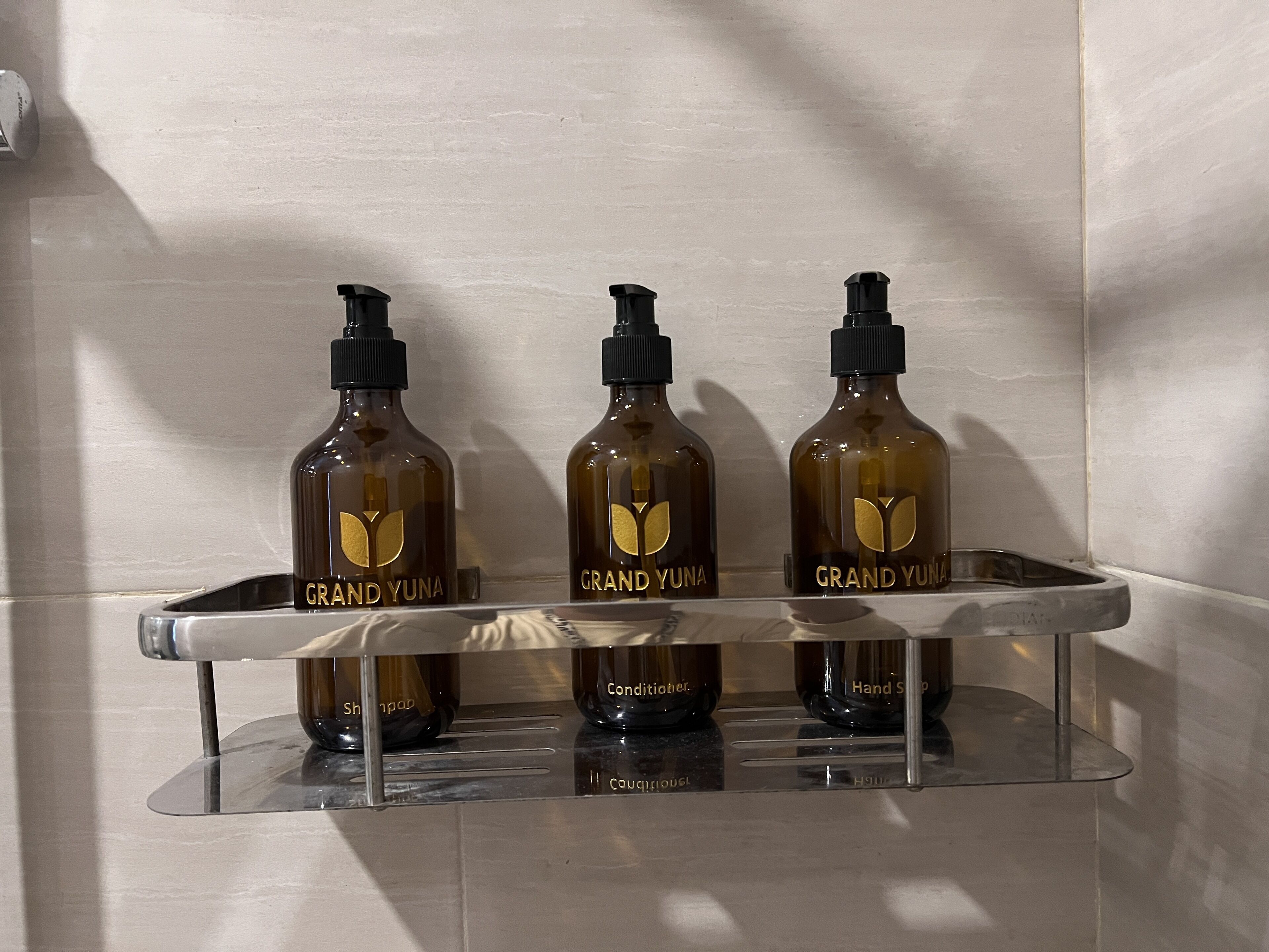 Three bottles of Grand Yuna conditioner on a clear shelf against a tiled wall.