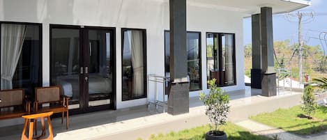 A modern building with large glass doors, a covered patio area with outdoor furniture, and a small garden.