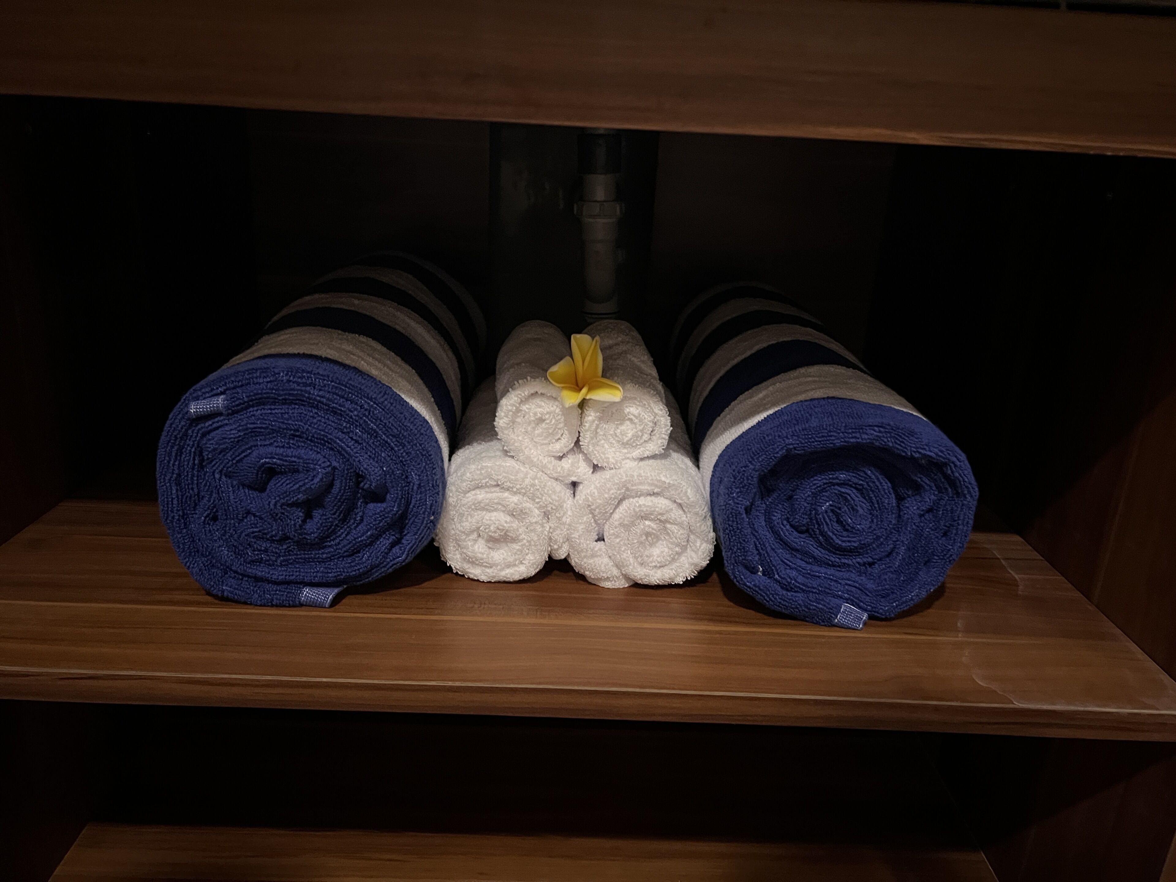 A wooden shelf with rolled towels in blue and white, some with yellow flowers.