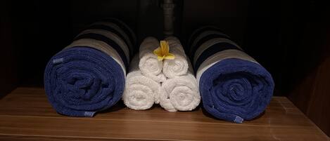 A wooden shelf with rolled towels in blue and white, some with yellow flowers.