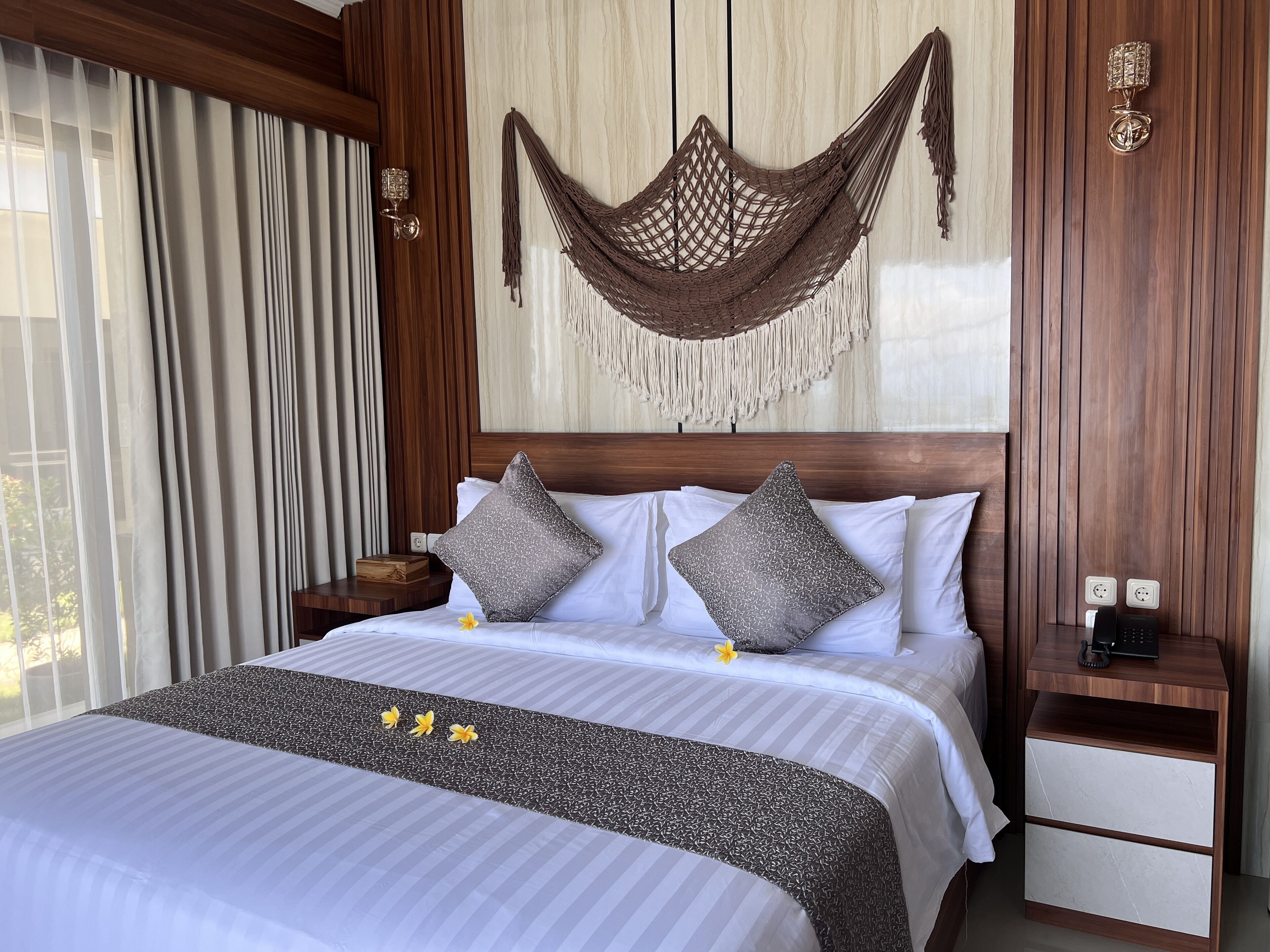 A hotel room with a large bed, two pillows, a nightstand, a wall-mounted lamp, and a wooden headboard.