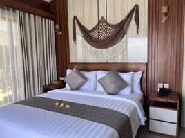 A hotel room with a large bed, two pillows, a nightstand, a wall-mounted lamp, and a wooden headboard.