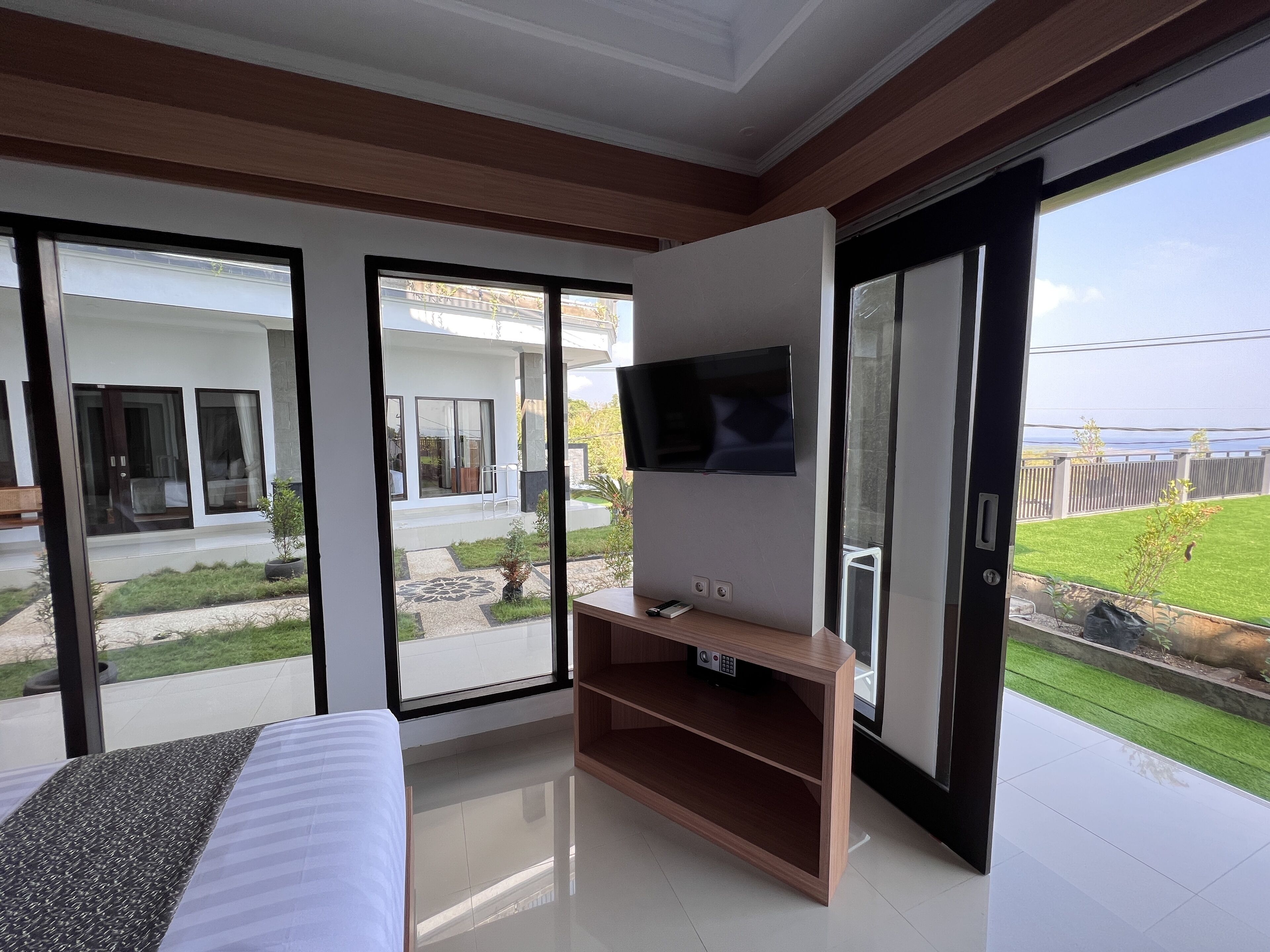 Ein modernes Zimmer mit Bett, Fernseher auf einem Holzboden und großen Schiebegläsern zum Balkon mit Meerblick.