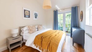 Een slaapkamer met een bed, nachtkastje, lamp en uitzicht op de omgeving door een raam.