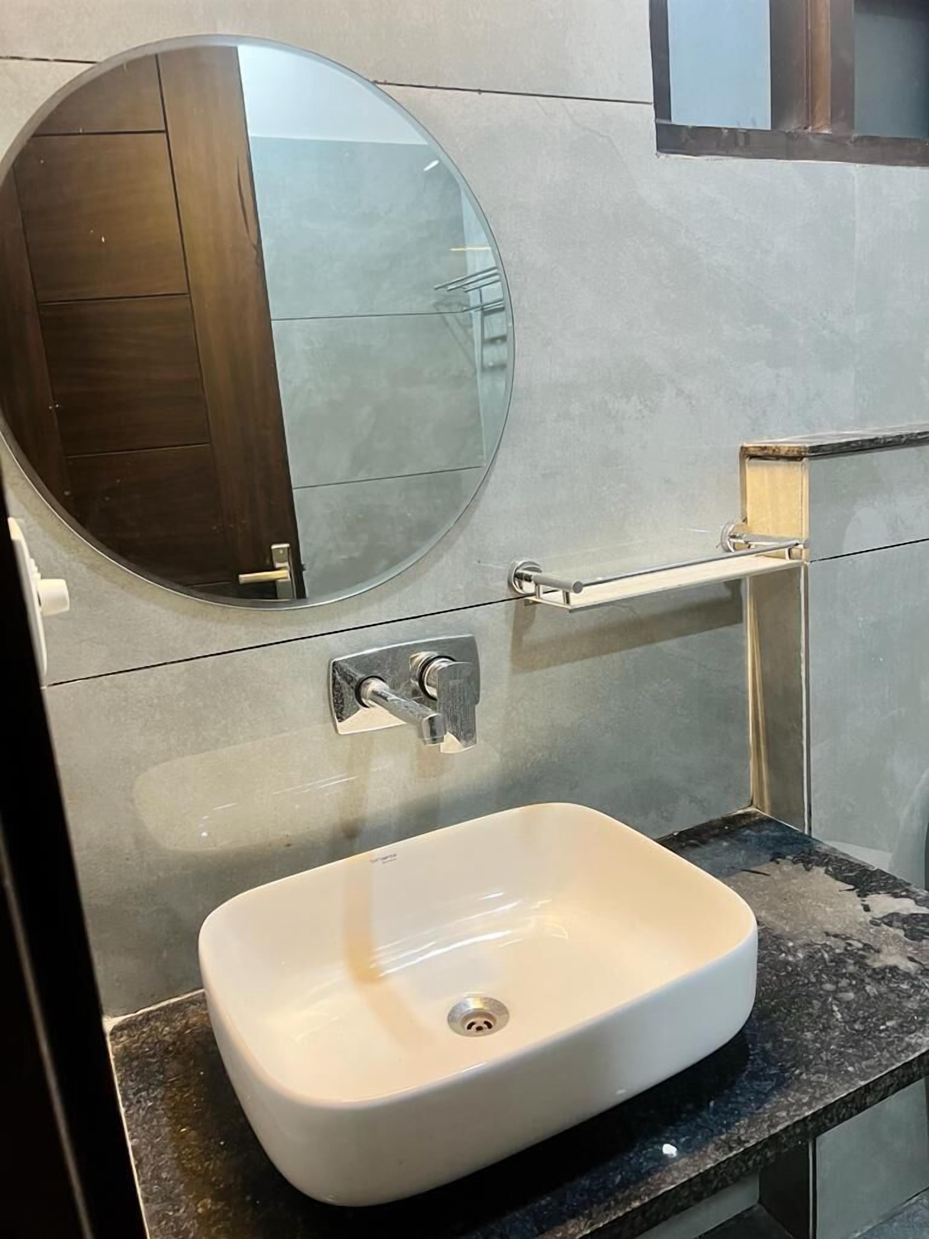 A bathroom with a round mirror, a white sink, and a towel rack.