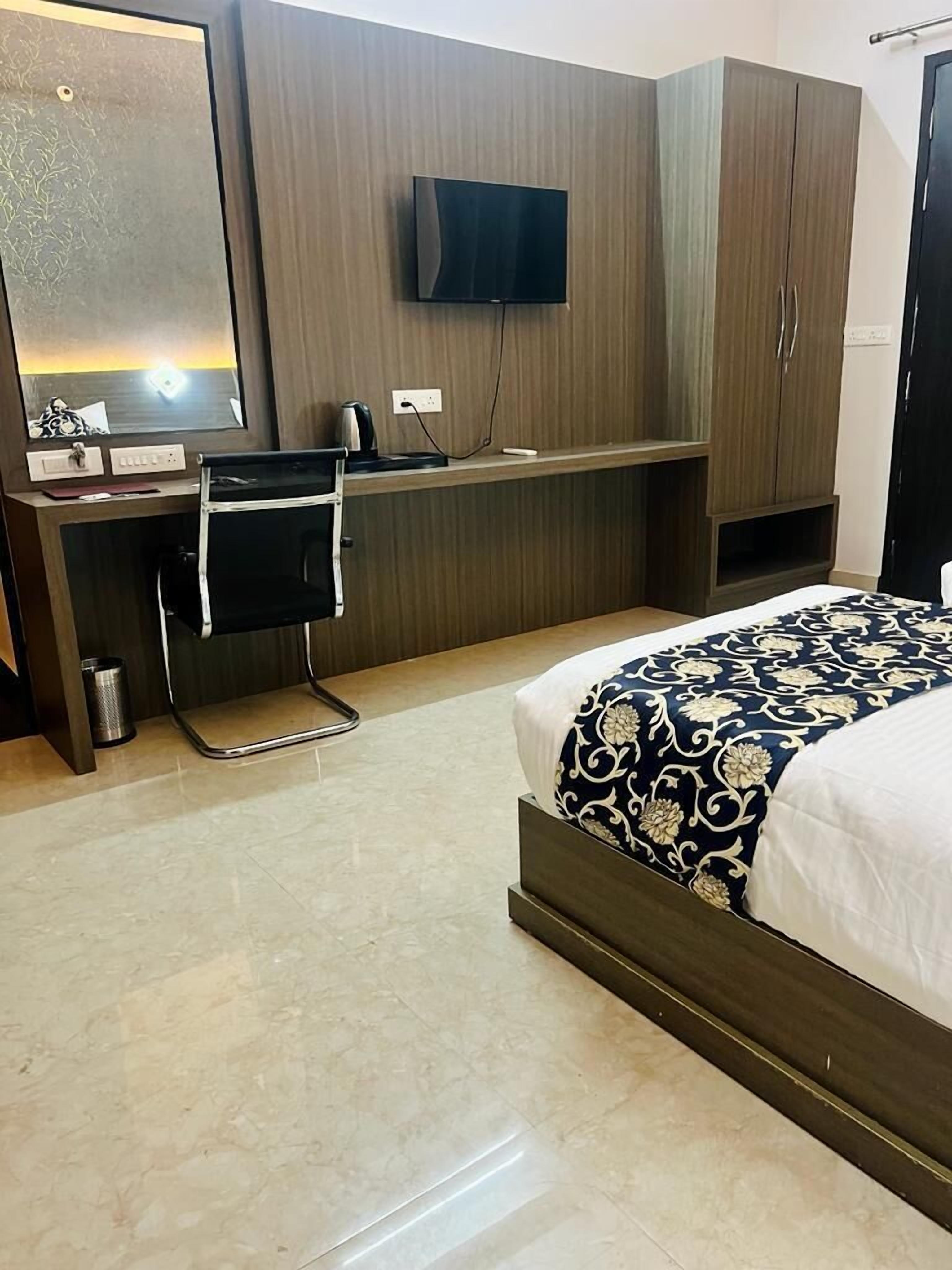 A hotel room with a bed, a desk, a chair, a television, and a wardrobe.