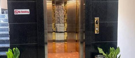 An elevator entrance with a "No Smoking" sign, marble flooring, and potted plants.