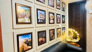A wall with framed pictures of various locations, a black leather sofa, and a decorative Buddha statue. - R G Bilkha Hotel And Resorts (Alwar)