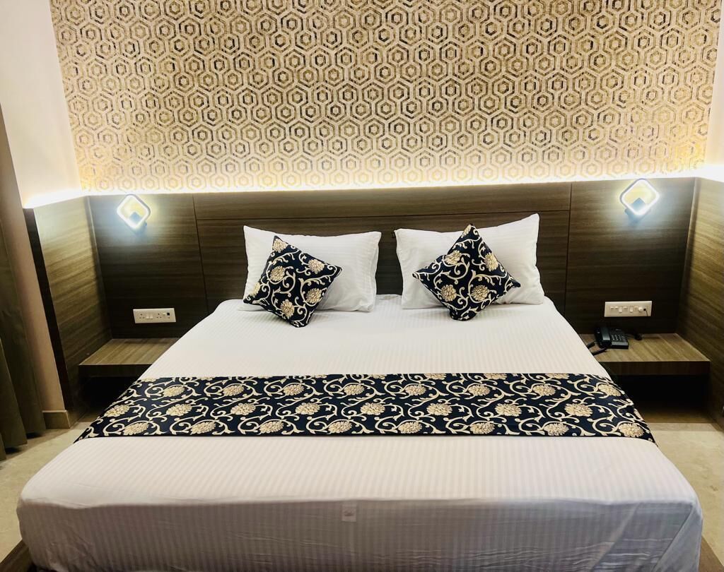 A hotel room with a neatly made bed, two bedside tables, and a patterned headboard.