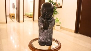 A statue of a figure in a robe on a glass table in a hotel lobby. - AVA Hotels and Corporate Stays Golf course (Gurugram)