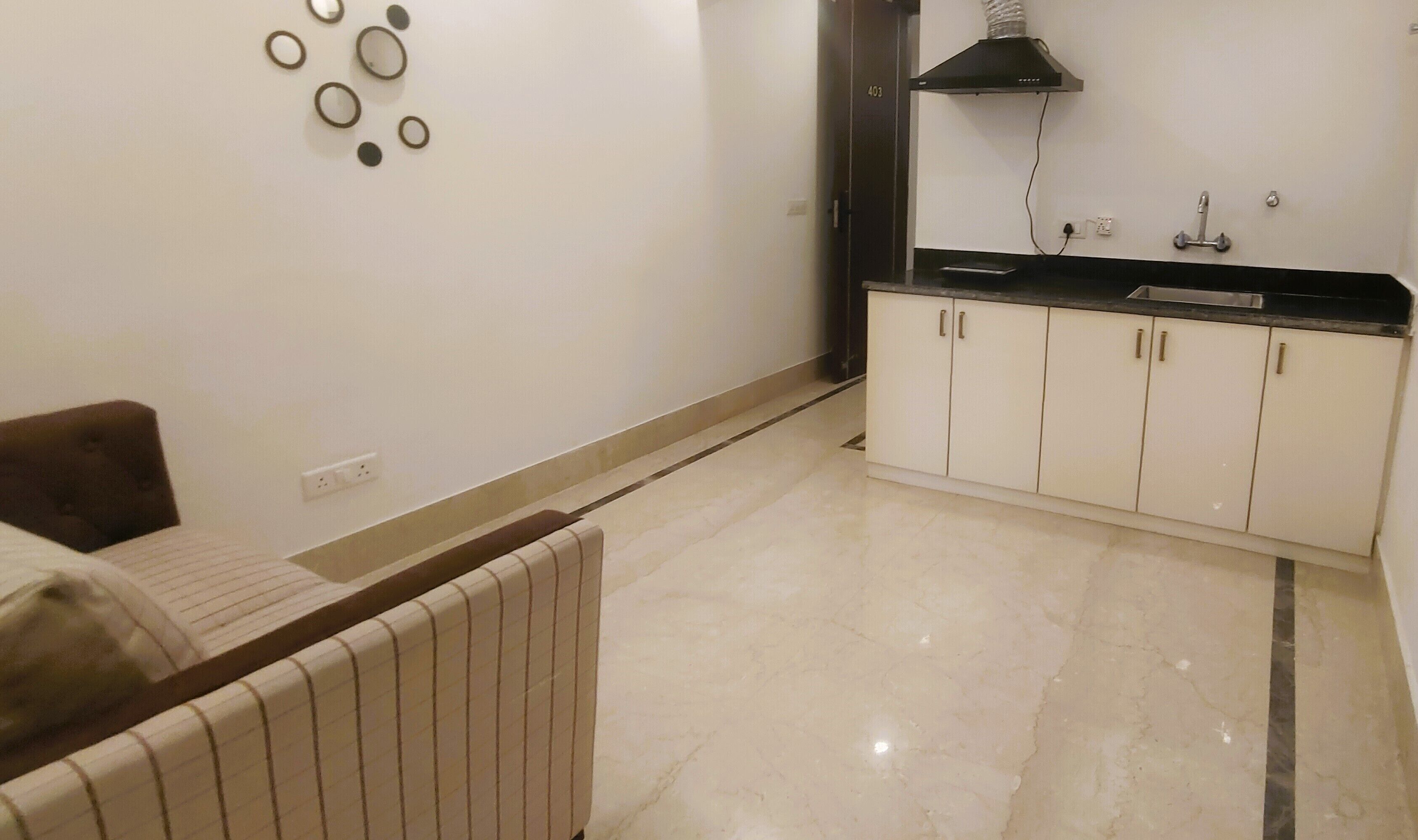 A small, clean room with a bed, a bedside table, a radiator, a white cabinet with a sink, and a wall-mounted mirror.