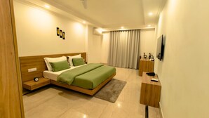A modern bedroom with a wooden bed, green bedding, a bedside table with a lamp, a small nightstand, a TV, and a window with curtains. - AVA Hotels and Corporate Stays Golf course (Gurugram)