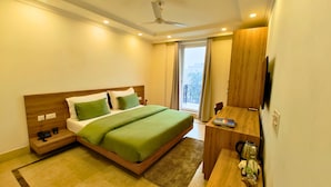 A modern hotel room with a wooden bed, green bedding, a small desk with a kettle, and a TV. - AVA Hotels and Corporate Stays Golf course (Gurugram)