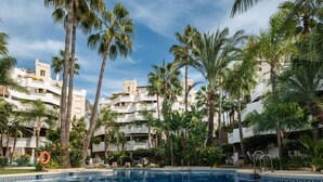 A swimming pool surrounded by palm trees and a multi-story building with balconies. - Fuente Aloha by Interhome (Marbella)