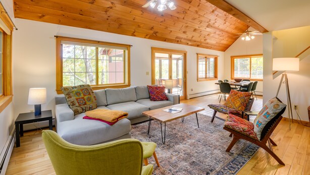 A spacious living room with a wooden ceiling, a sofa, a coffee table, and a chair. - Charming Putney Home: Porch, Grill & Hiking Trails (Putney)