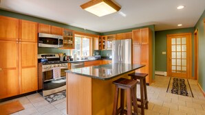 A kitchen with wooden cabinets, a central island, a refrigerator, a stove, and a microwave. - Charming Putney Home: Porch, Grill & Hiking Trails (Putney)