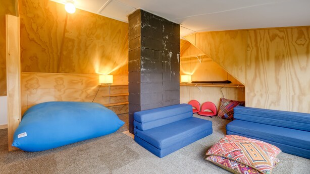 Een gezellige kamer met een houten plafond, een zwarte pilaar en een blauwe zithoek.