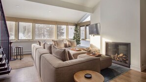 Un salon moderne avec un grand canapé d’angle, une cheminée et une grande fenêtre donnant sur un paysage enneigé.