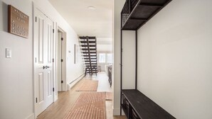 Un couloir aux murs blancs, doté d’un plancher en bois et d’un escalier en métal noir. Deux tapis sont posés sur le sol et un panneau d’accueil est accroché au mur.