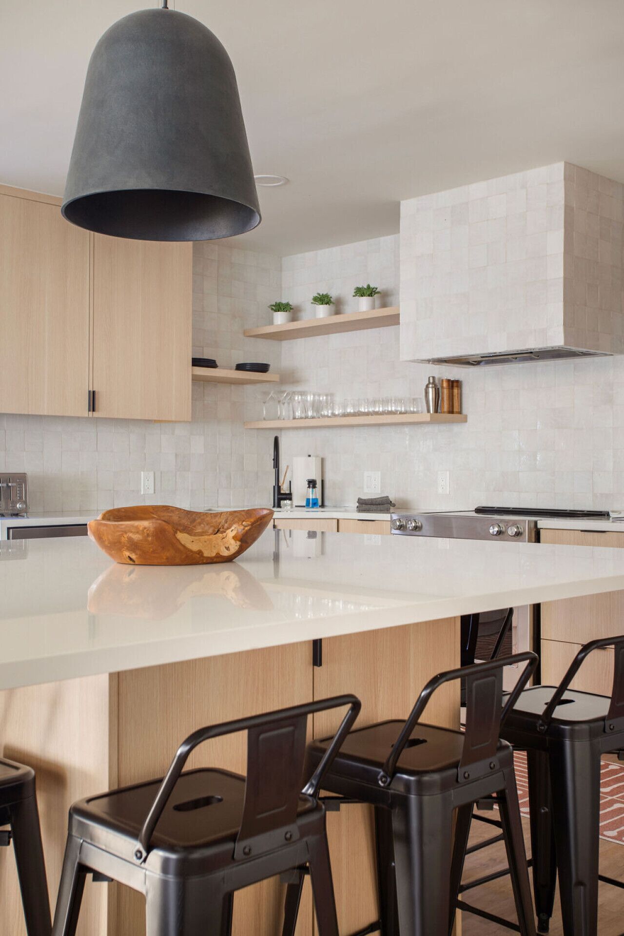 A modern kitchen with a large island, wooden cabinets, and a black pendant light.