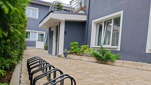 A building with a grey exterior, a paved walkway, and a row of black metal bike racks. - Lovely Scandinavian style studio in Riga (Rīga)