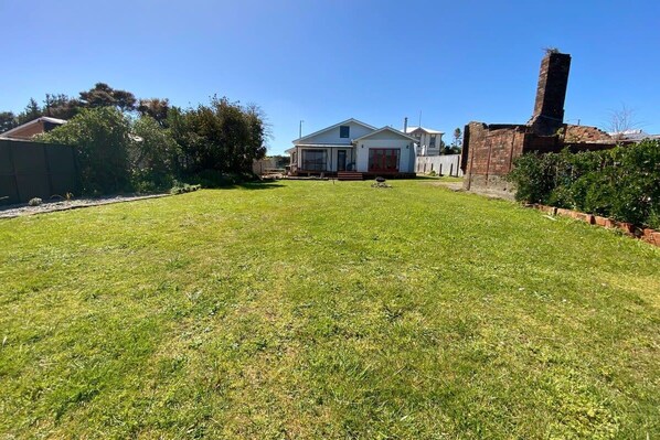 A residential property with a well-maintained lawn, a detached house with a chimney, and a brick structure to the right.