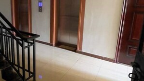 A spacious hallway with a tiled floor, wooden doors, and a staircase with black railings.